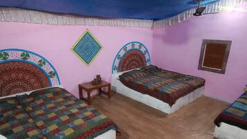 A room with three beds, each with a patterned bedspread. There is a small table and a wall hanging.