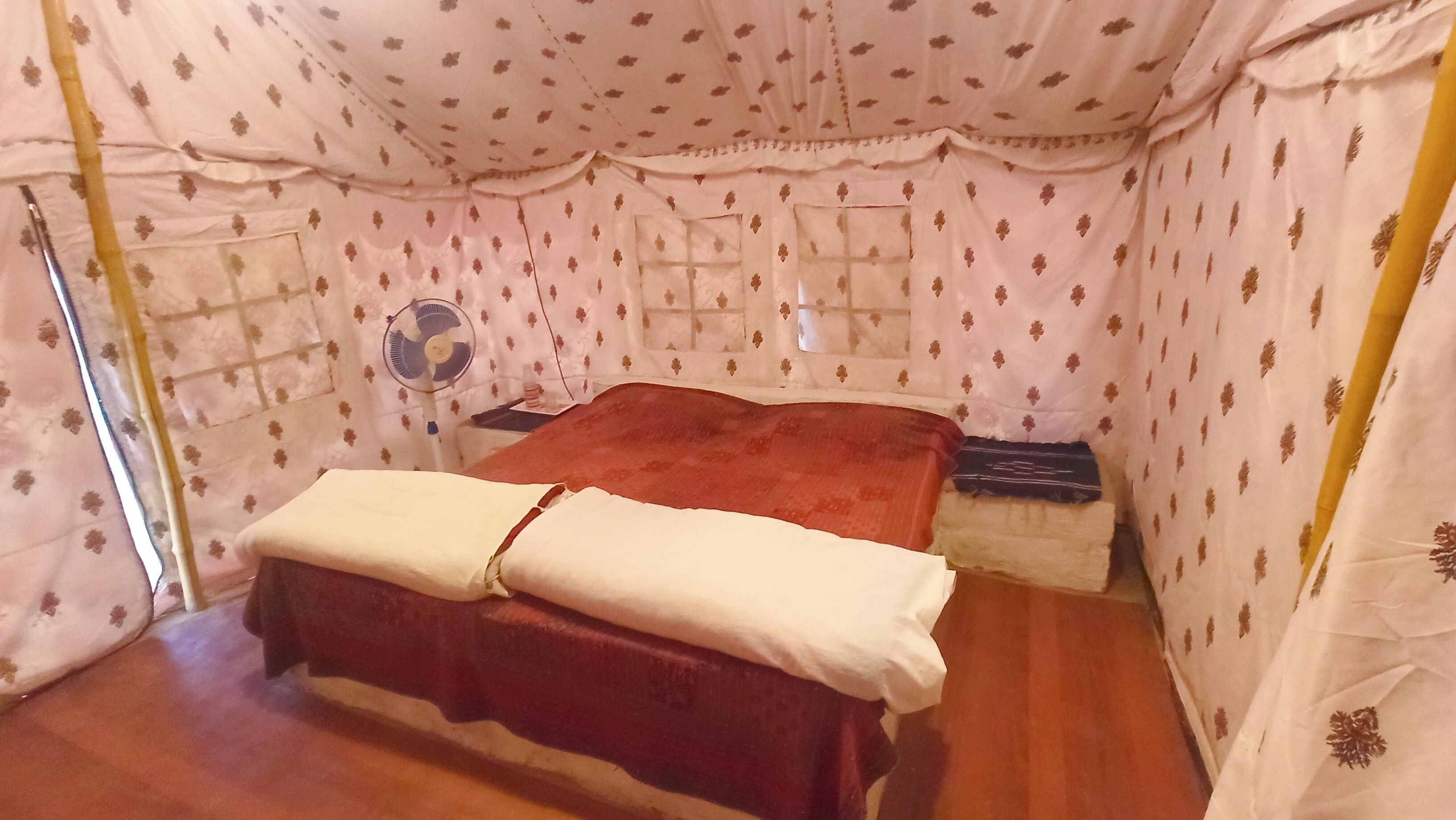 A tent-style room with a bed, a fan, and a small table.