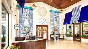 Zona de recepción de un hotel con un mostrador curvo, una recepcionista y un gran ventanal con cortinas estampadas azules.
