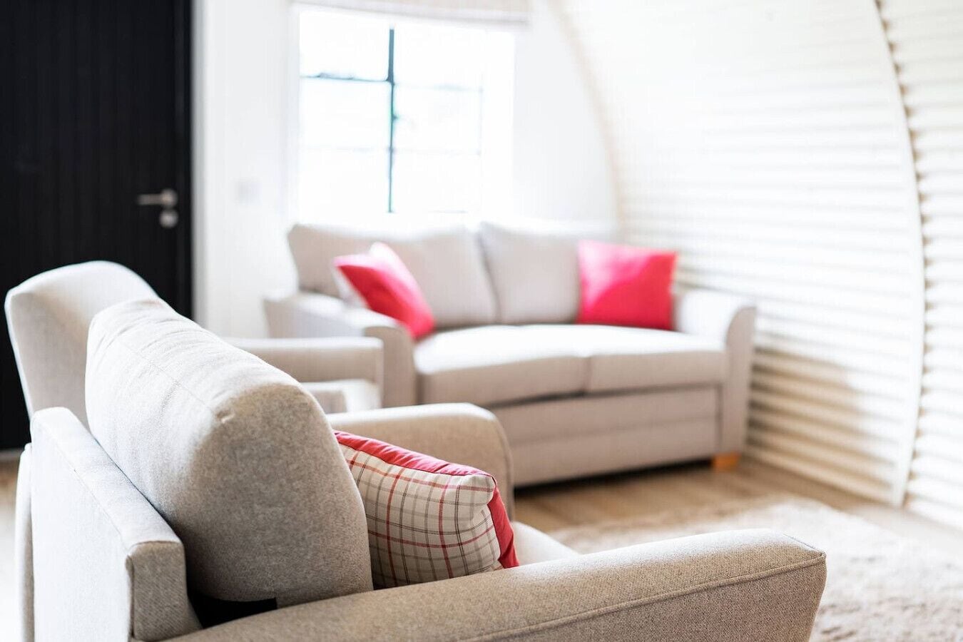 A living room with two sofas, one with a red and white checkered pillow, and a window with blinds.