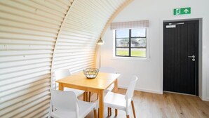 Una habitación con techo curvo, una mesa de madera con sillas blancas, una ventana con vistas y una puerta con letrero de salida de emergencia.