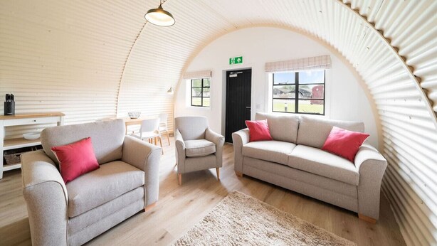 Una sala de estar acogedora, con techo abovedado, piso de madera, dos sofás, un sillón y una mesa.