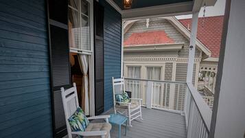 A covered porch with two white rocking chairs and a small table, overlooking a building with a red roof.