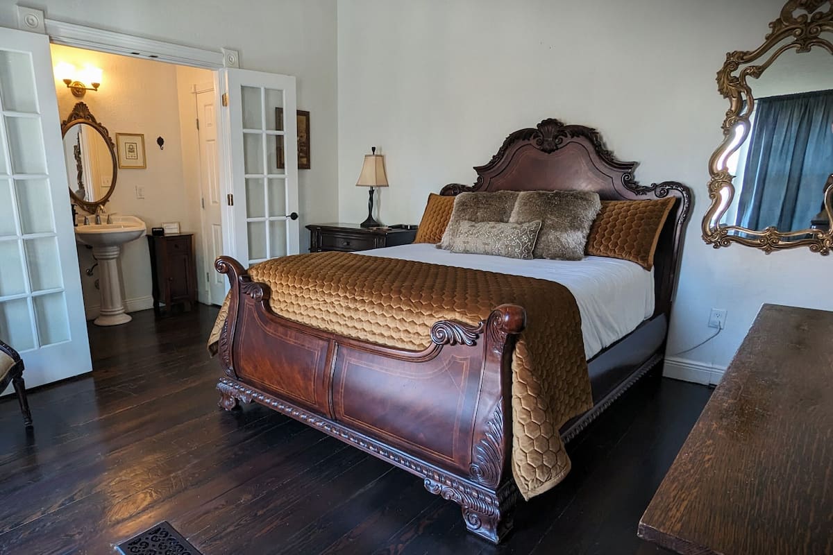 A traditional bedroom with a four-poster bed, a sitting chair, a dresser, and a mirror.