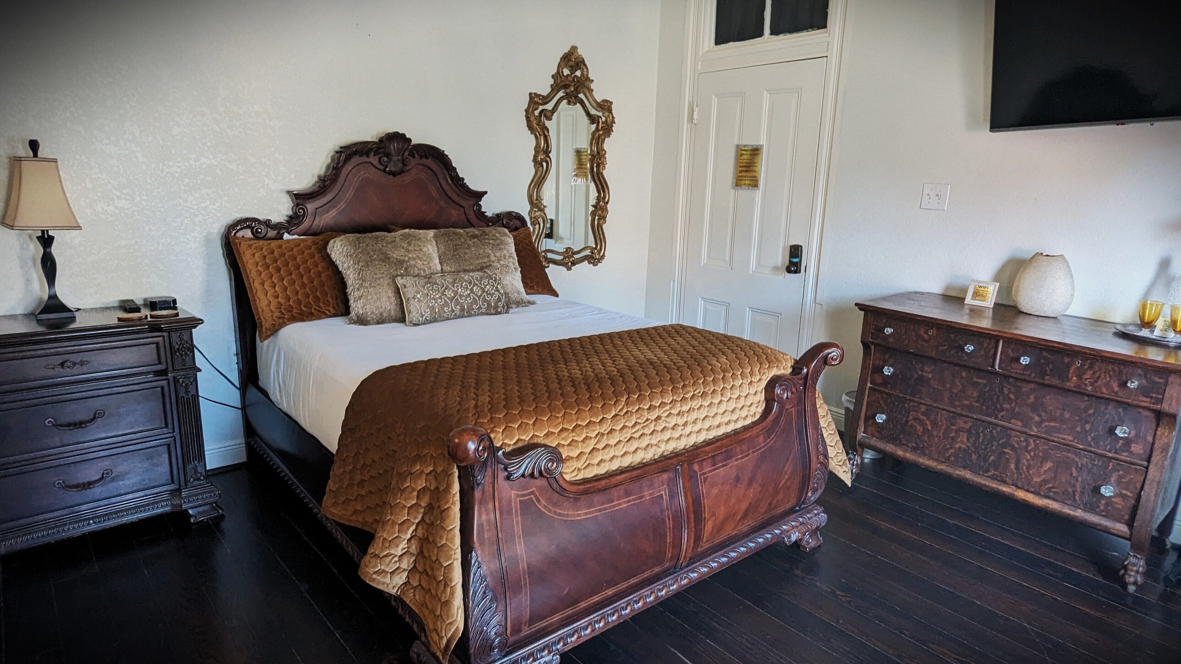 A traditional bedroom with a wooden bed, a dresser, a mirror, and a lamp.