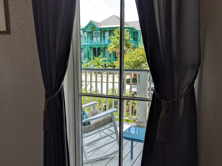 A room with a sliding glass door leading to an outdoor deck with a white rocking chair and a small table.
