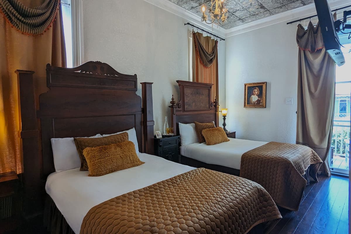 A hotel room with two beds, wooden headboards, and a chandelier.