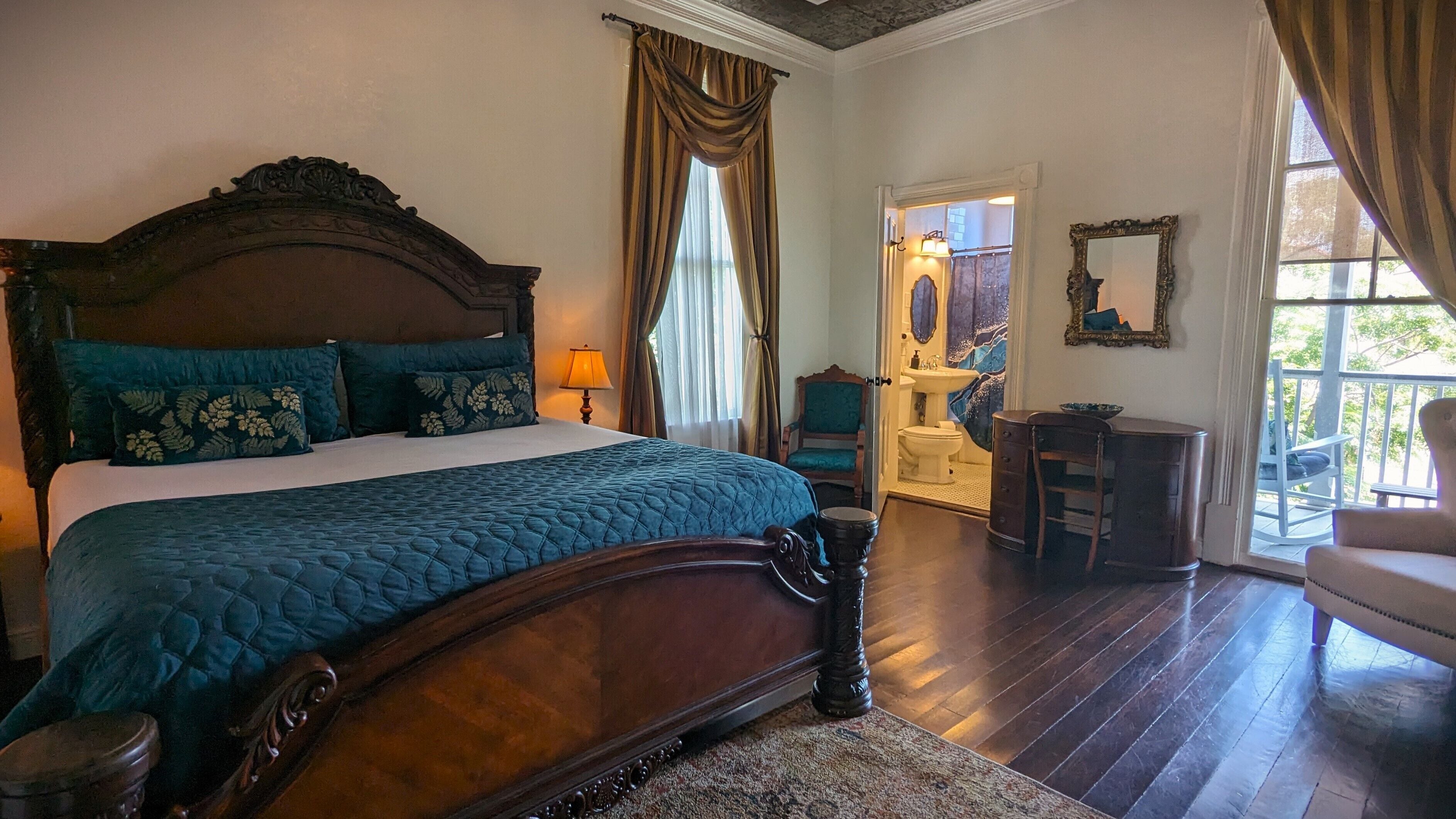 A bedroom with a large bed, a wooden headboard, and a view of the bathroom through an open door.