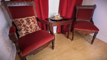 Duas cadeiras de madeira ornamentada com estofamento vermelho e uma pequena mesa com um tabuleiro que contém um copo e uma placa.