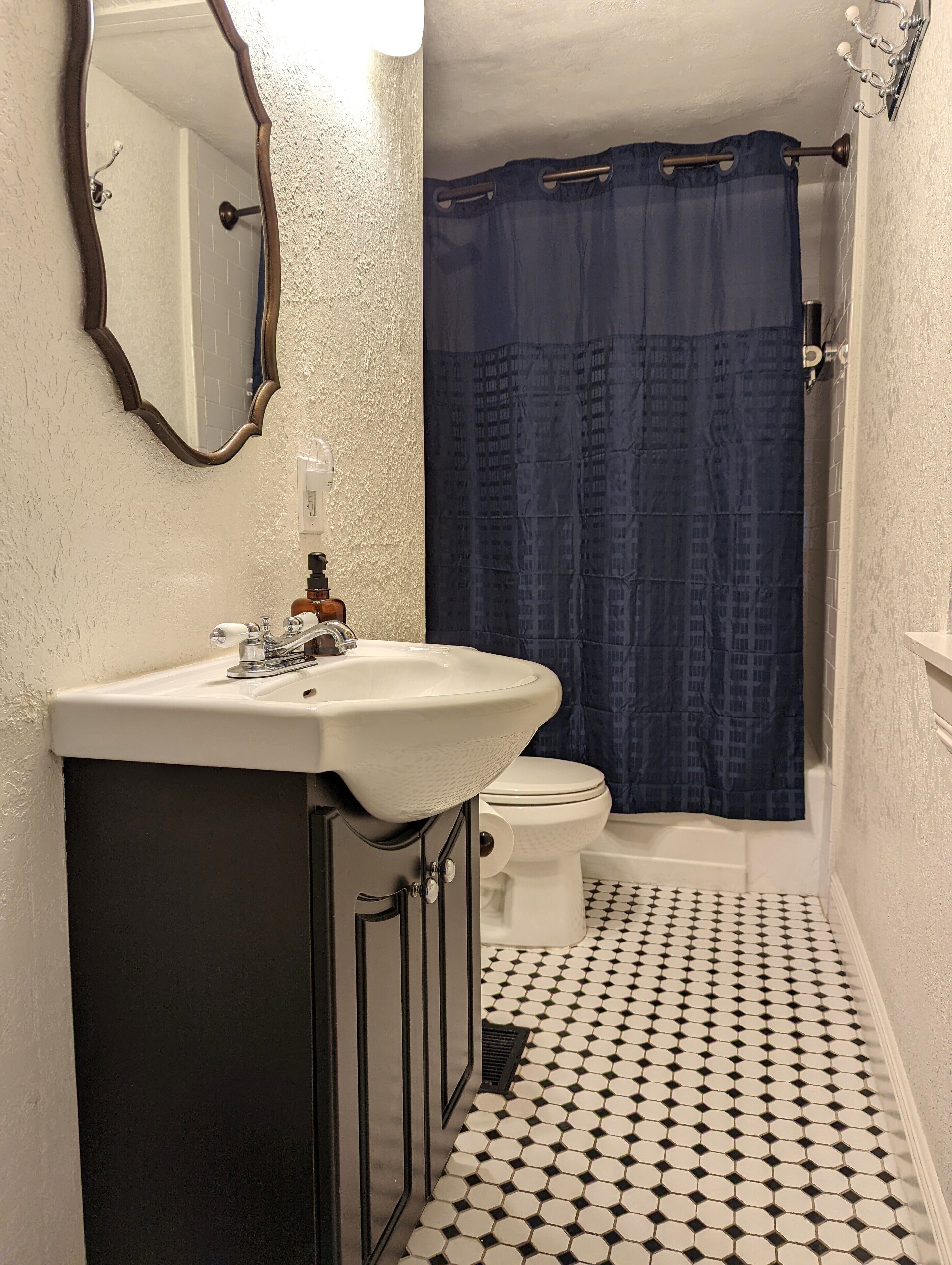 A bathroom with a white sink, a toilet, and a shower with a blue curtain. The floor has a black and white checkered pattern.