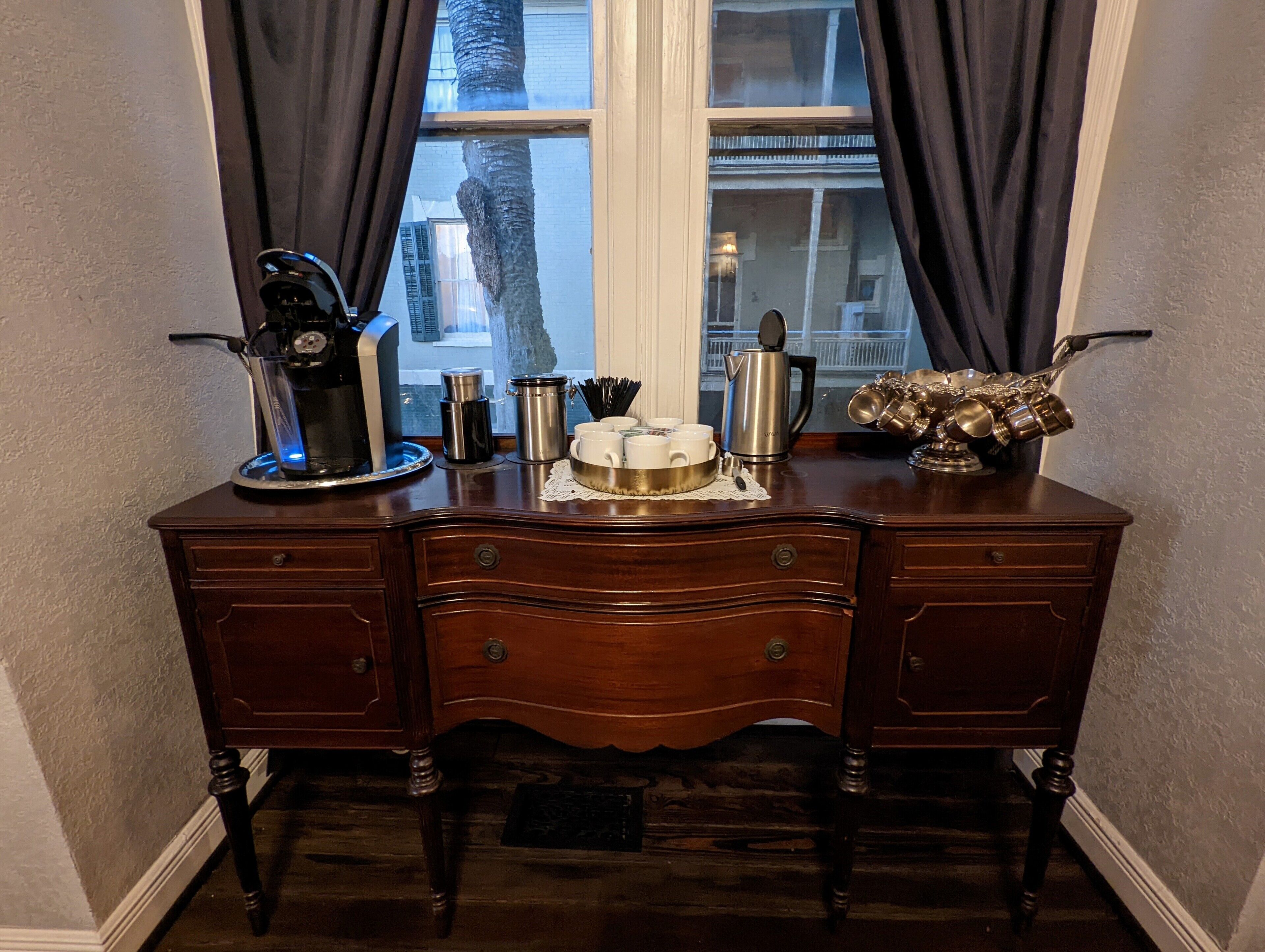 A wooden desk with a coffee maker, cups, and a teapot.