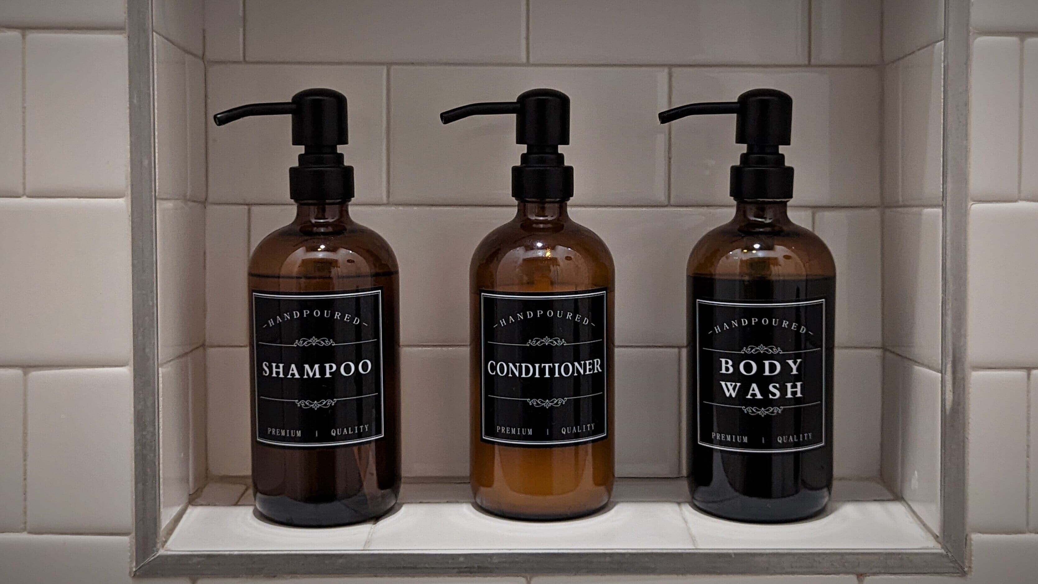 Tres botellas de champú, acondicionador y jabón de baño hechas a mano en un estante de baño.
