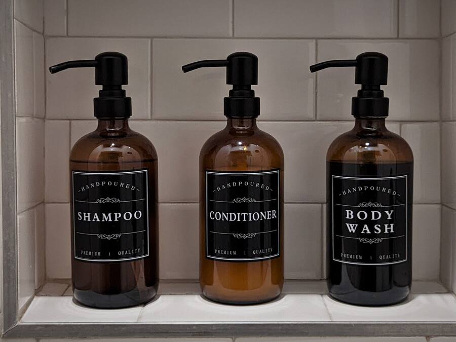 Tres botellas de champú, acondicionador y jabón de baño hechas a mano en un estante de baño.