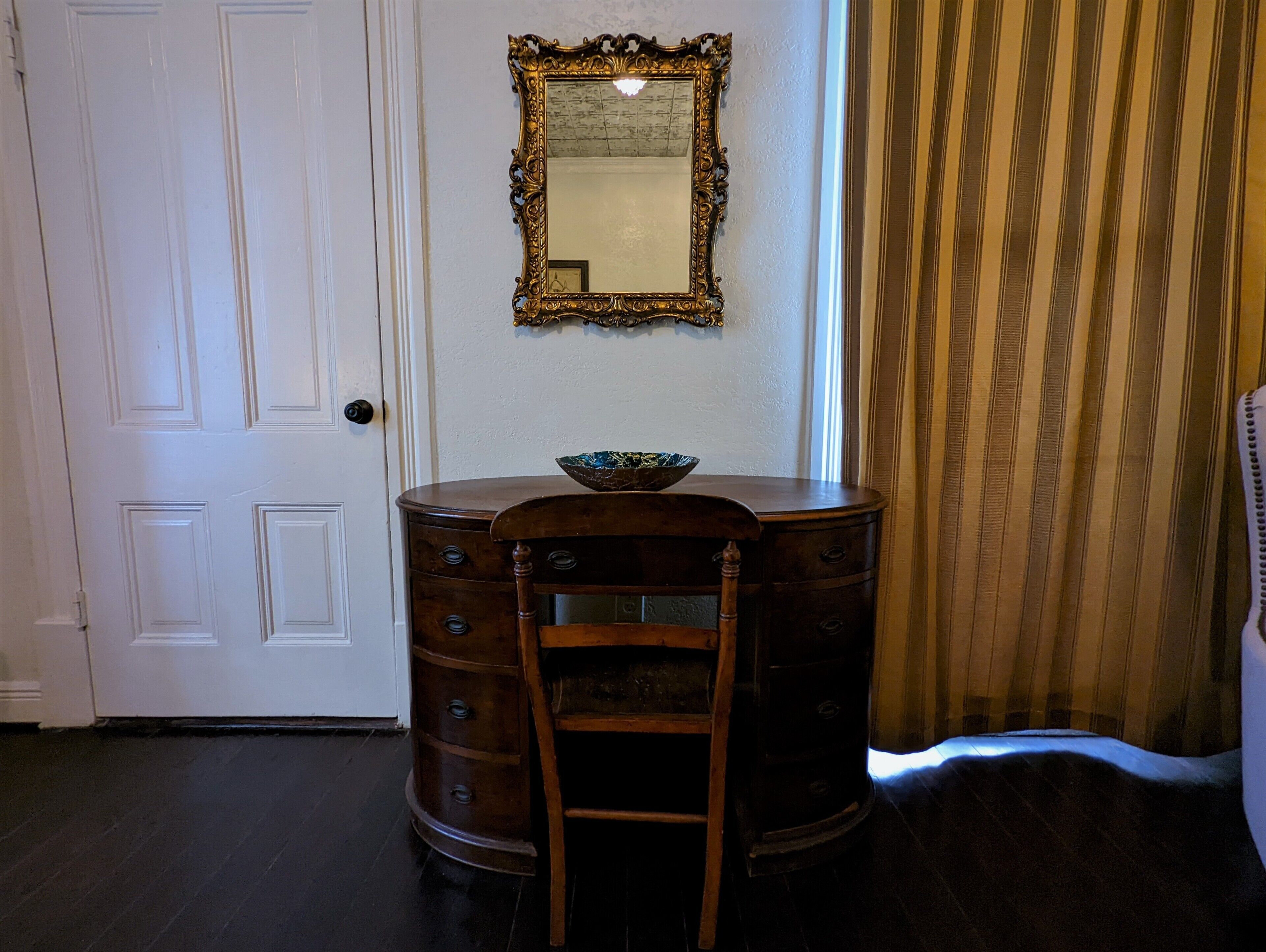 A room with a wooden dresser, a chair, a mirror, and a striped curtain.