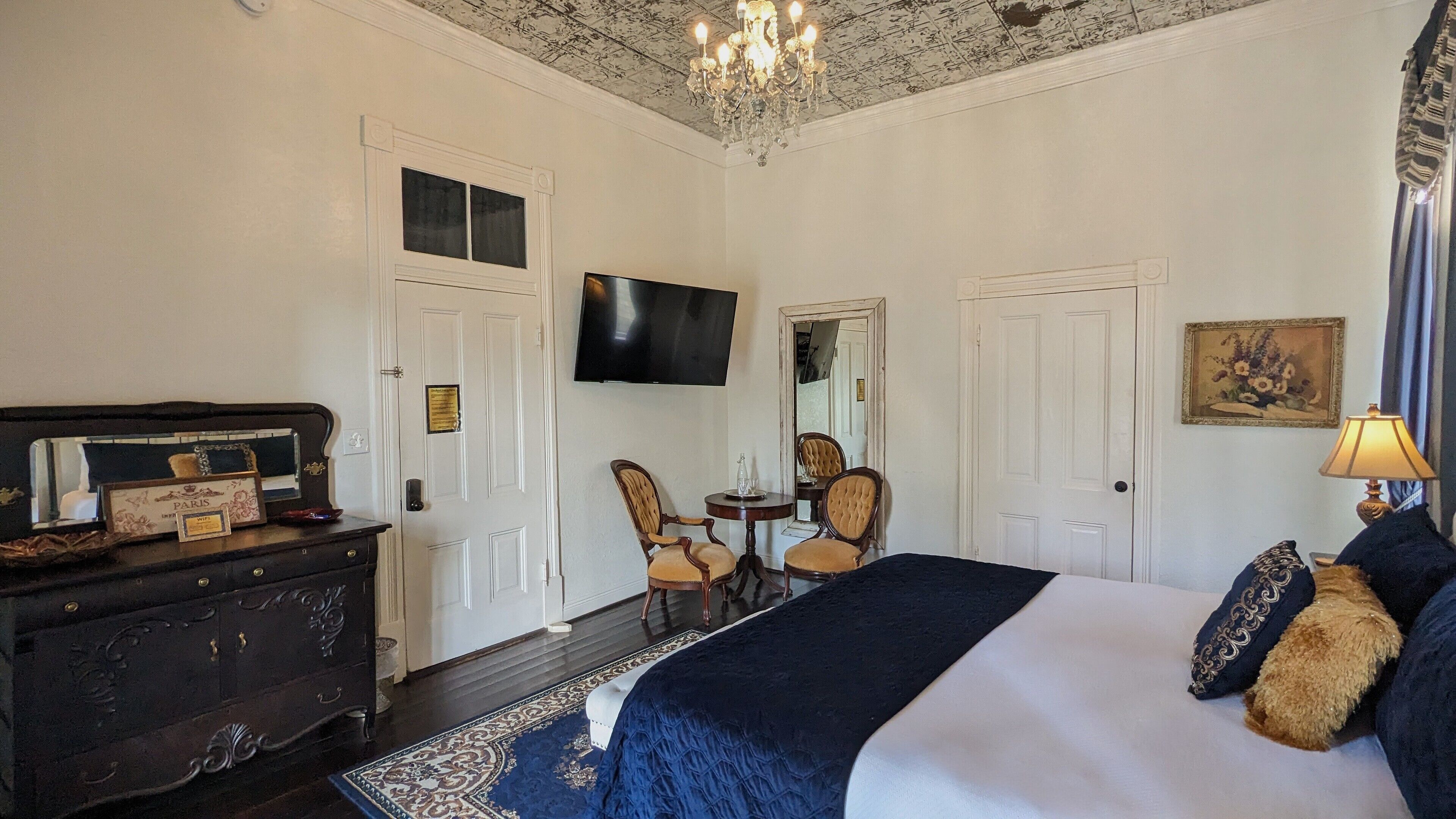 A bedroom with a large bed, a dresser, a TV, and a chandelier.