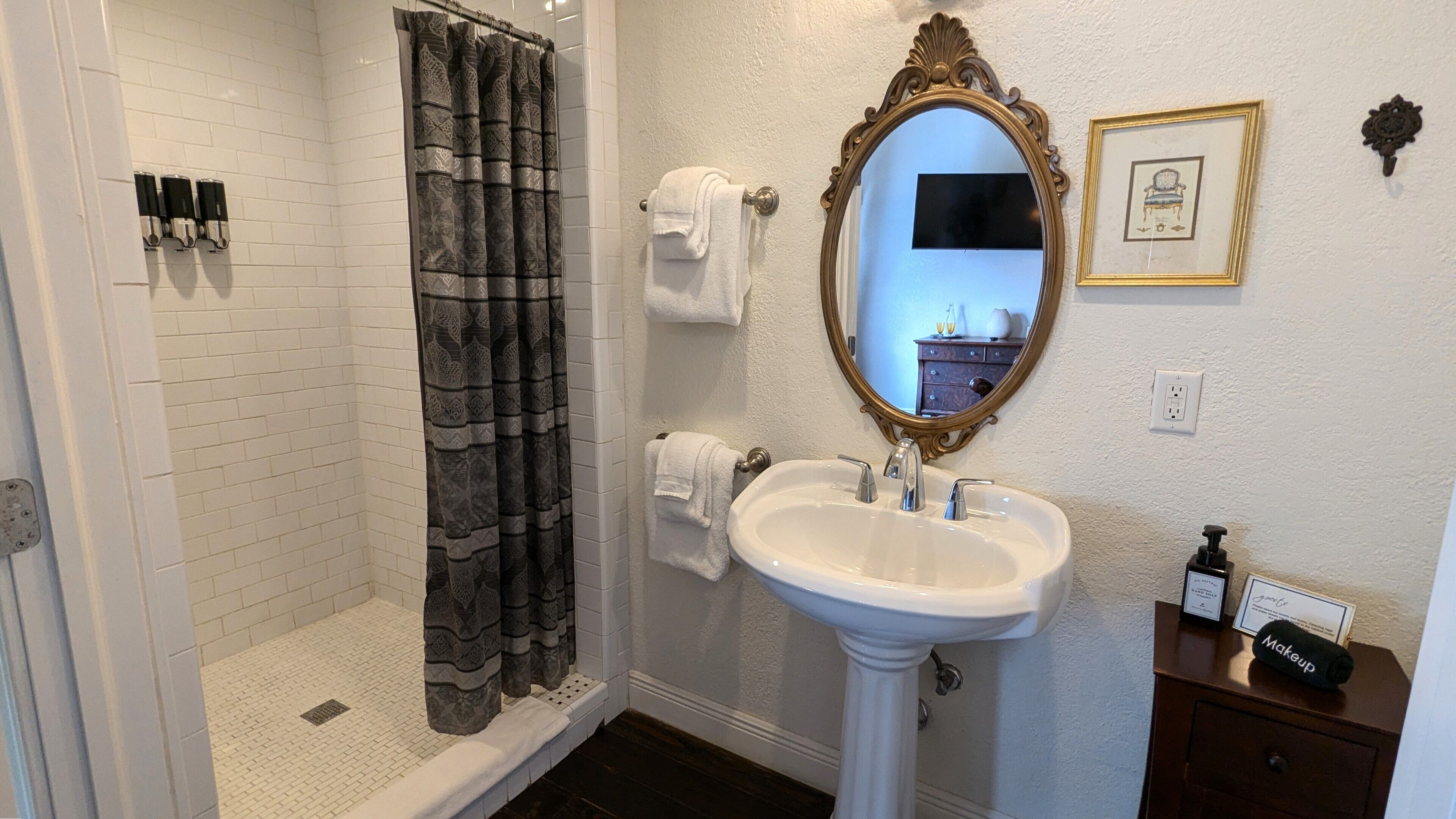 A bathroom with a shower, a sink, a mirror, and a vanity with toiletries.