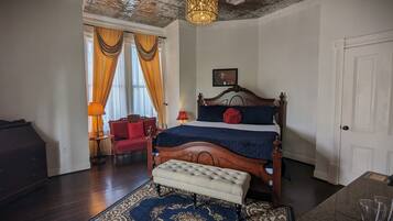 A bedroom with a large bed, a bench, a chair, a lamp, and a chandelier.
