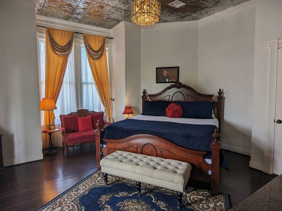 A bedroom with a large bed, a bench, a chair, a lamp, and a chandelier.
