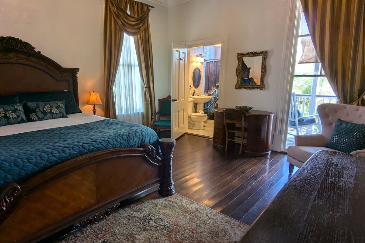 A bedroom with a large bed, a dresser, a chair, and a bathroom visible through an open door.