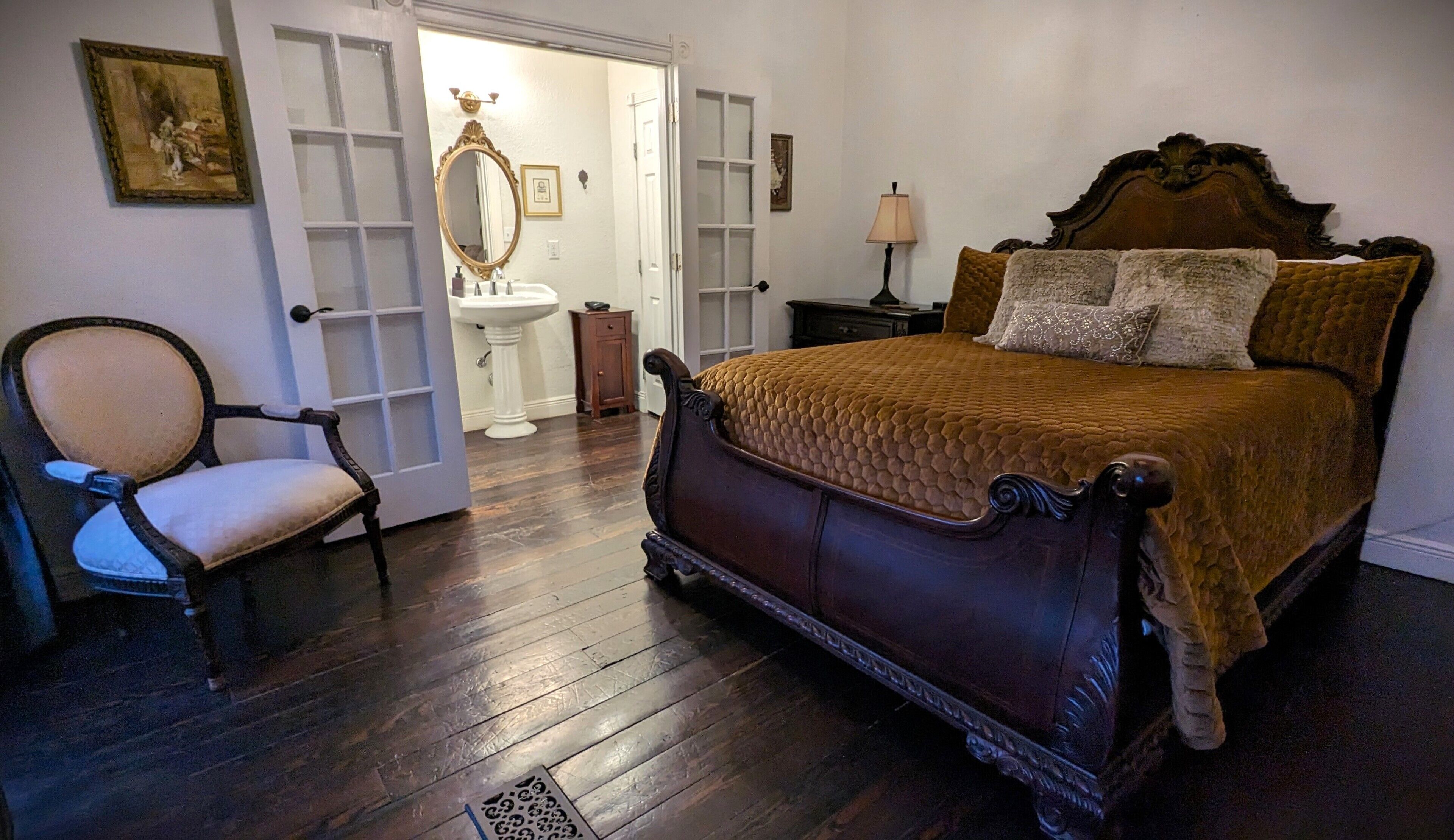 A bedroom with a large bed, a chair, a dresser, a mirror, and a door leading to another room.