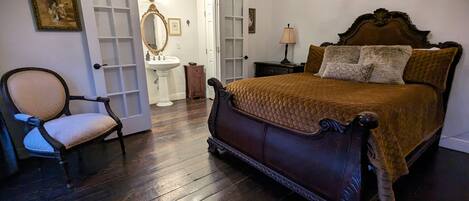 A bedroom with a large bed, a chair, a dresser, a mirror, and a door leading to another room.