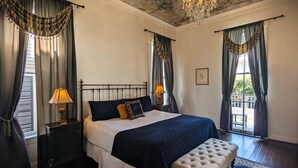 A bedroom with a bed, two bedside tables, a bench, a chandelier, and curtains.