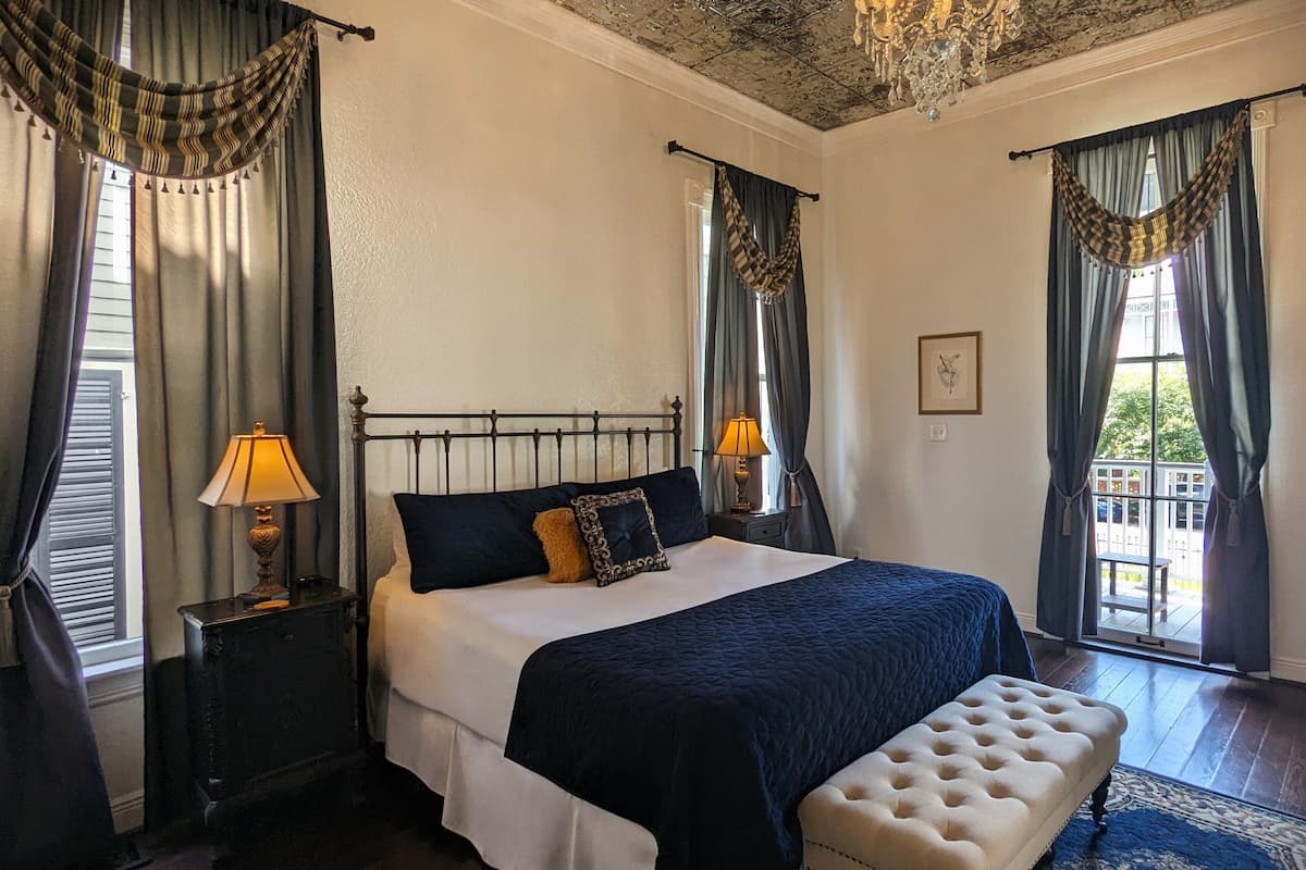 A bedroom with a bed, two bedside tables, a bench, a chandelier, and curtains.