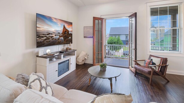 Un salon comprenant un grand téléviseur à écran plat, un canapé, une table basse et un fauteuil. Une porte-fenêtre coulissante donne accès à un balcon offrant une vue sur le quartier.