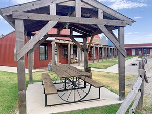 A wooden pavilion with a picnic table in front, set against a backdrop of a red building with multiple rooms and a sign that reads "CROFT".