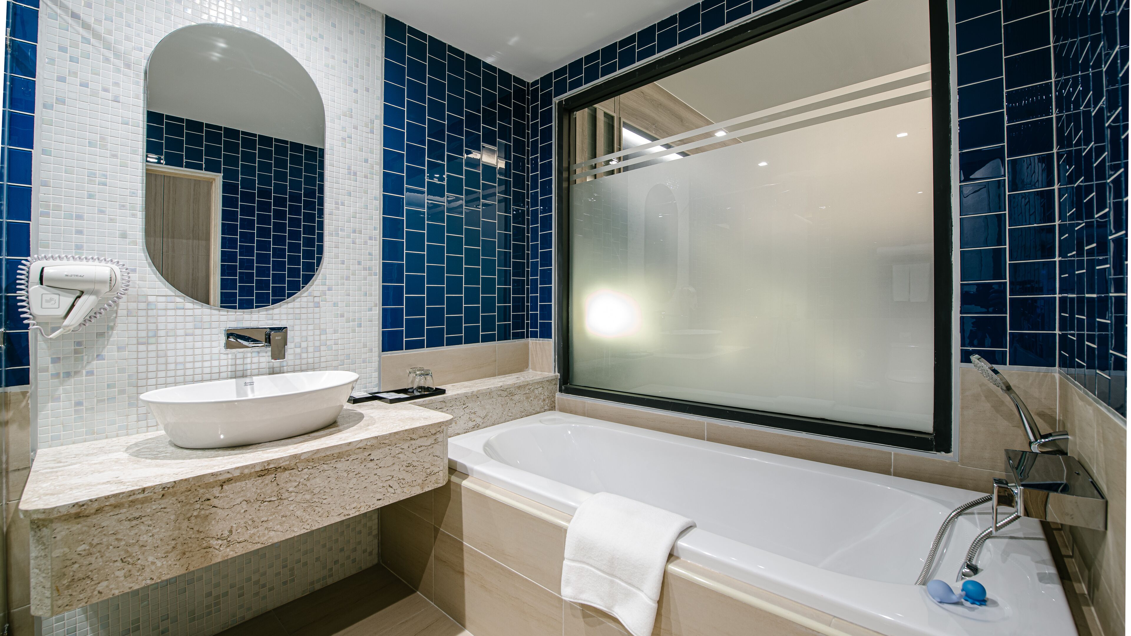 Un baño moderno con una bañera grande, un espejo redondo y un lavabo blanco.