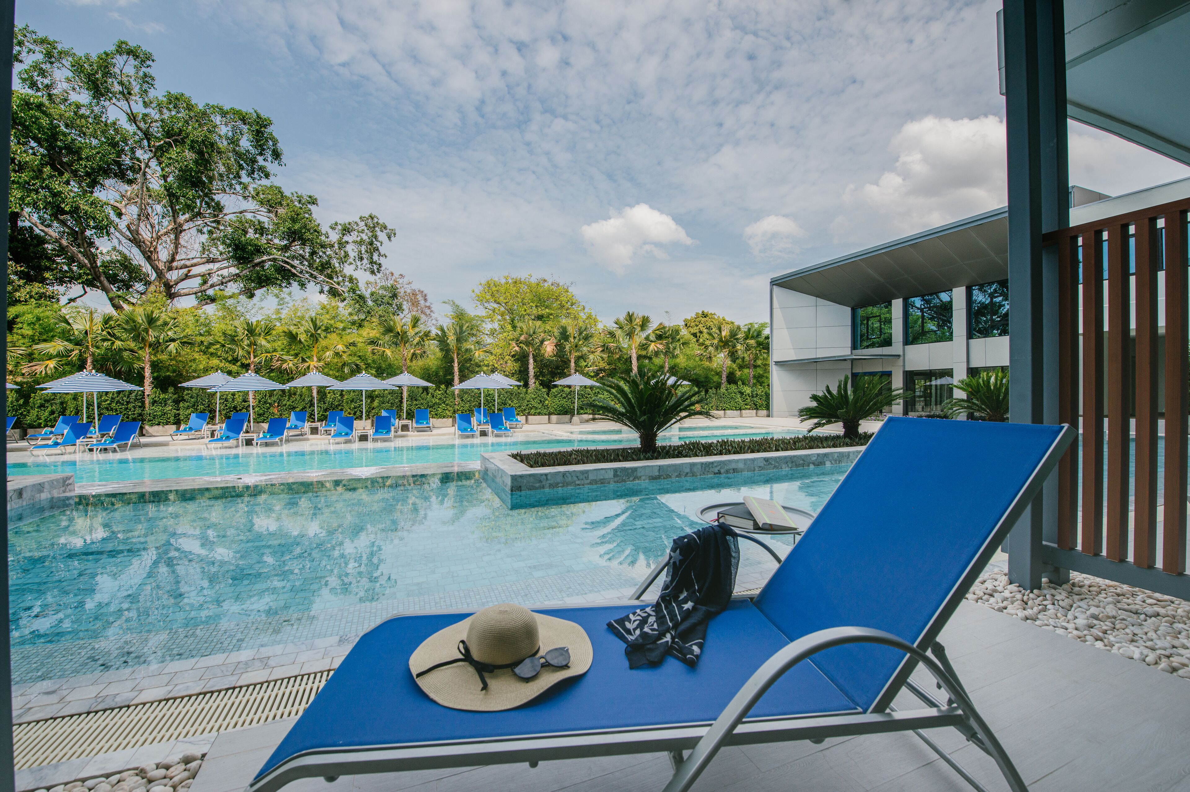 A pool area with blue lounge chairs, a hat, and sunglasses on one chair.