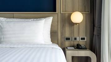A neatly made bed with white linens, a bedside table with a lamp, a phone, and a small book.