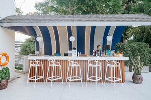 Zona de bar con taburetes blancos, una barra y una persona de pie detrás.