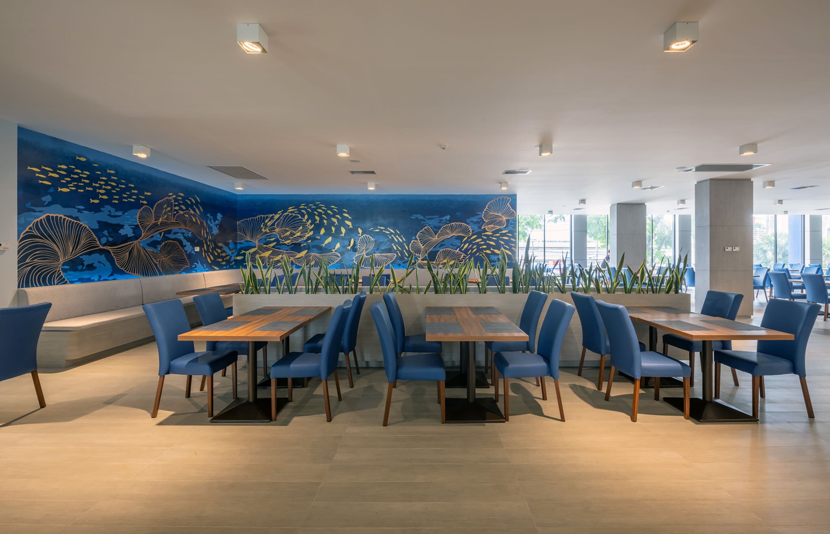 Un restaurante moderno con un gran mural de vida marina en la pared, sillas azules y mesas de madera.