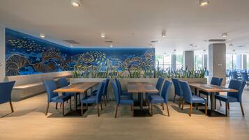 Un restaurante moderno con un gran mural de vida marina en la pared, sillas azules y mesas de madera.