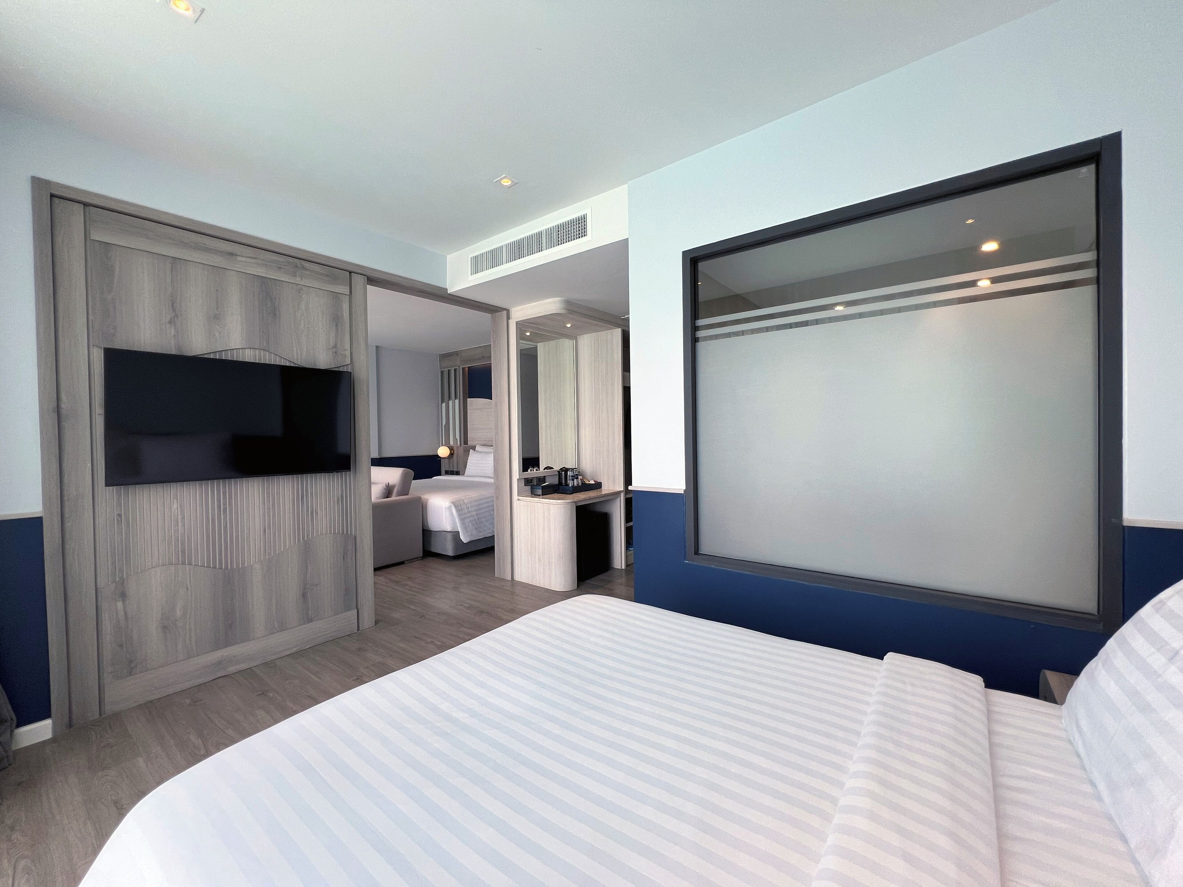 Ein modernes Hotelzimmer mit einem großen Bett, einem an der Wand befestigten Fernseher, einem Schreibtisch mit Stuhl und einem großen Fenster.
