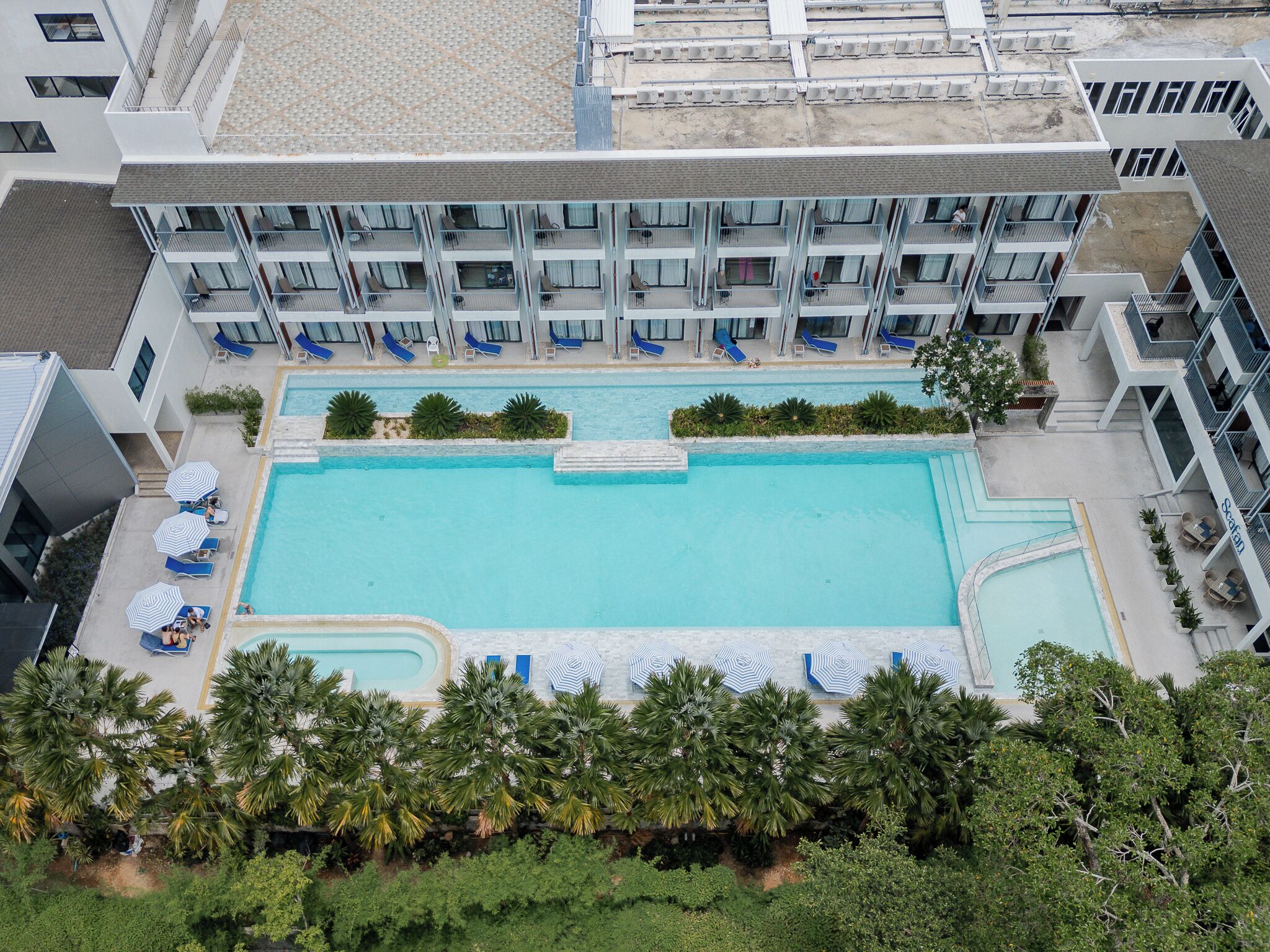 Un hotel con piscina en la azotea, varios balcones y un jardín paisajístico.