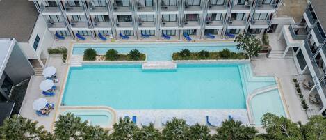 Un hotel con piscina en la azotea, varios balcones y un jardín paisajístico.