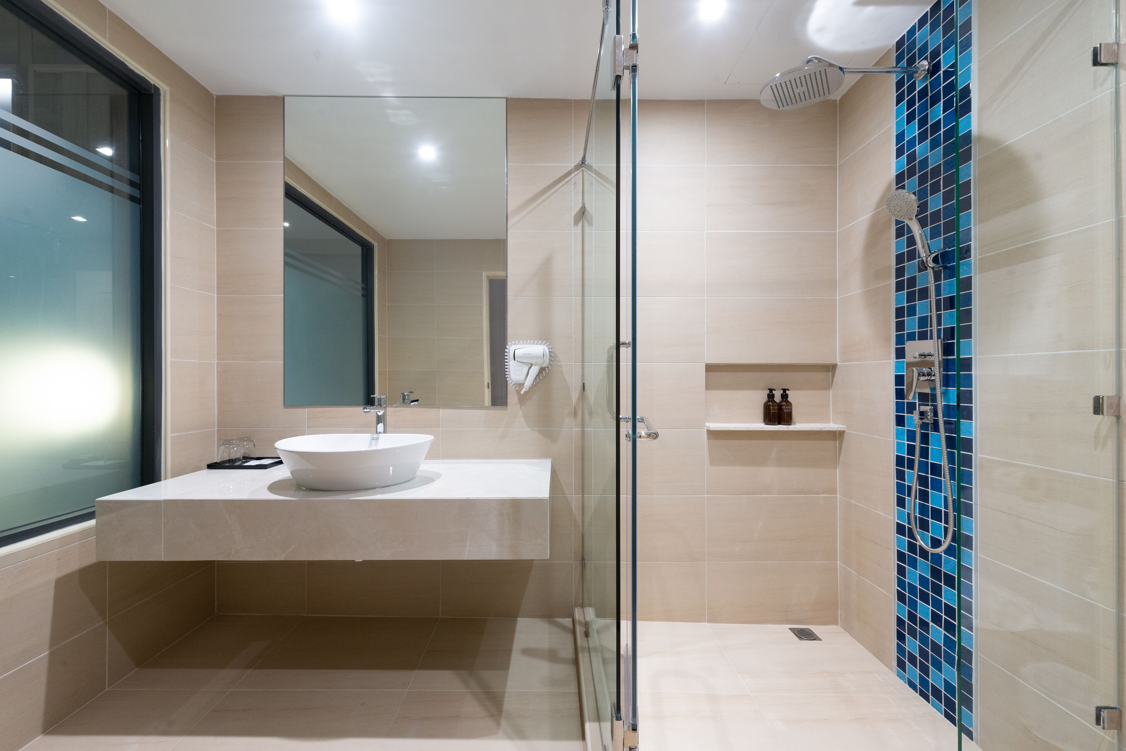 A modern bathroom with a glass-enclosed shower, a white sink, and a tiled wall with blue accents.