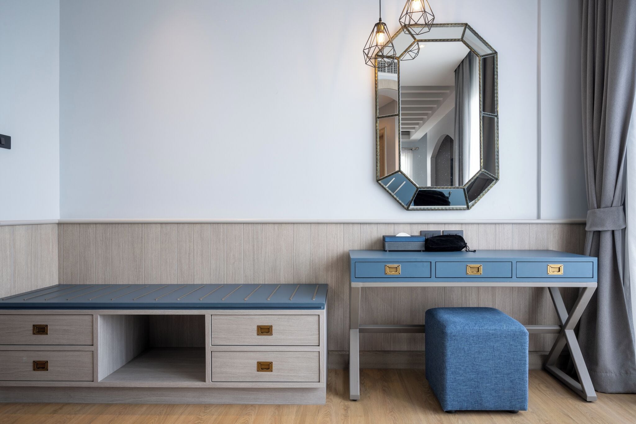 A modern bedroom with a bed, a desk with drawers, a mirror, and a hanging light fixture.
