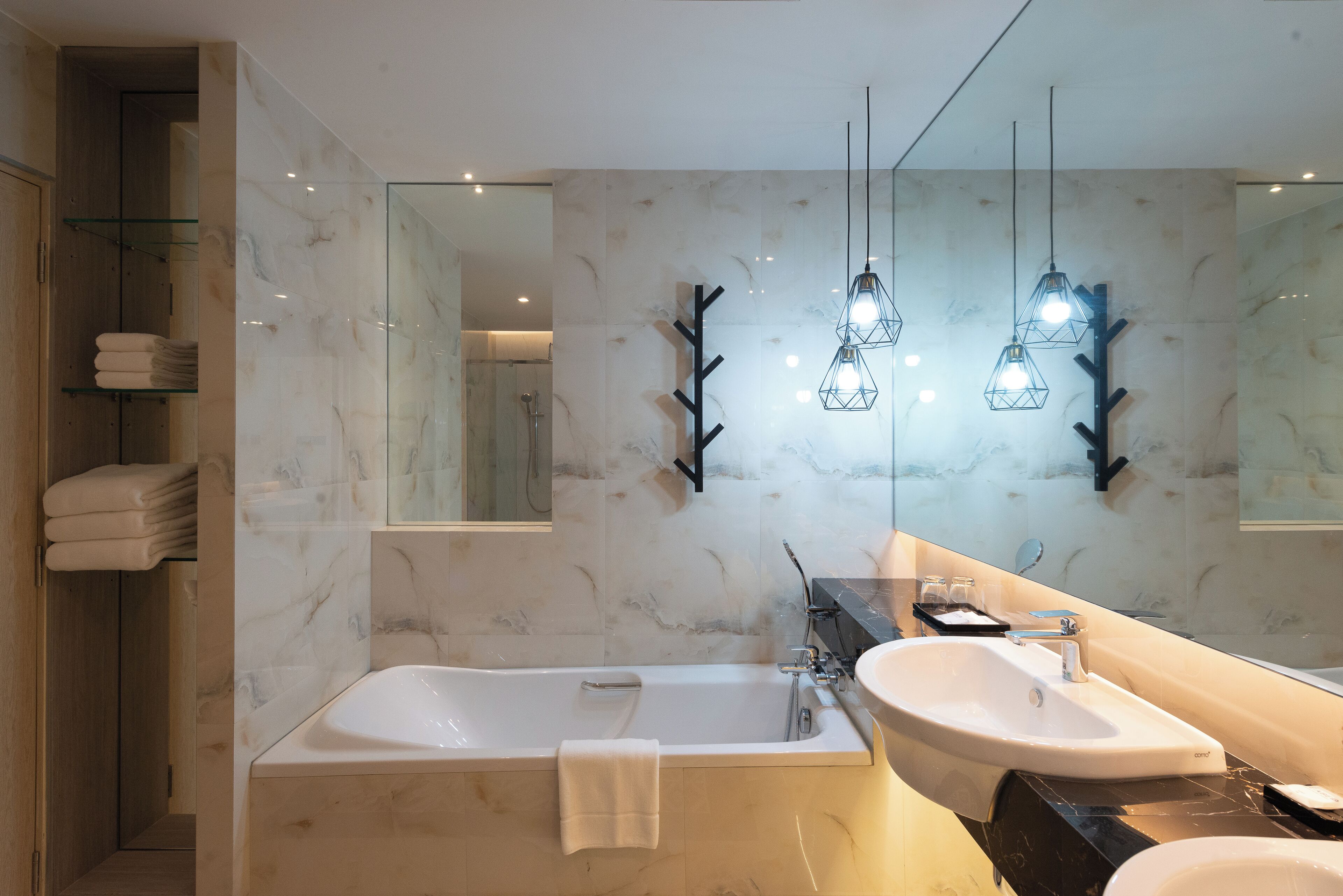 Un baño moderno con una bañera grande, un tocador con lavamanos y un espejo. Hay toallas apiladas en un estante, y lámparas colgantes sobre el espejo.