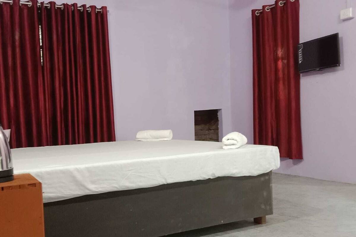 Un dormitorio con cama, cortinas rojas, una toalla blanca y televisión en la pared.