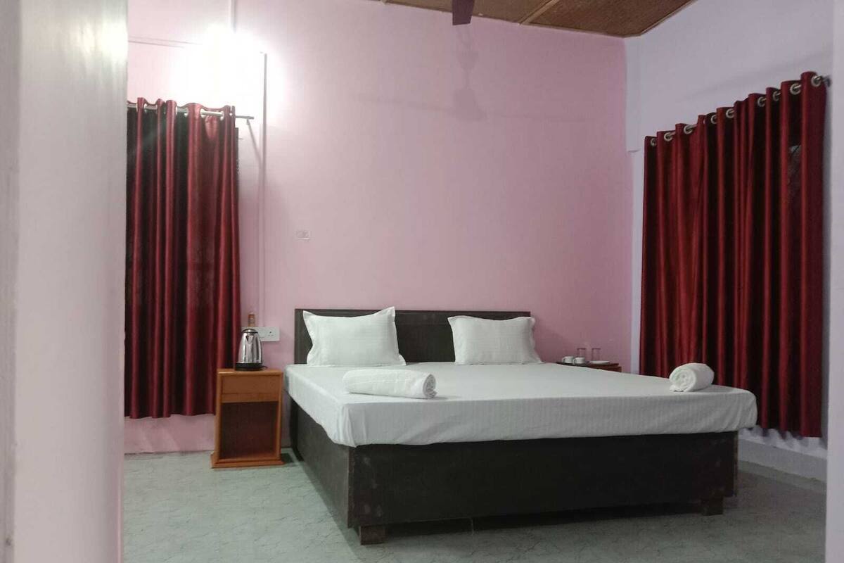 Un dormitorio con cama, mesita de noche, lámpara y cortinas rojas.