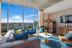 A modern living room with a city view, a large flat-screen TV, and a mix of contemporary and classic furniture. - Big Bend - Rooftop pool & gym on Rainey Street (Austin)