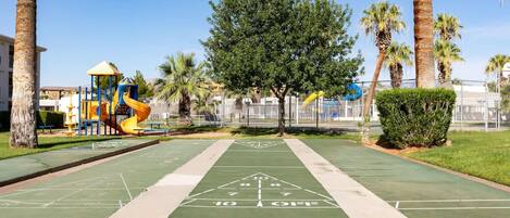 A park with a playground, a green shuffleboard court, and palm trees.