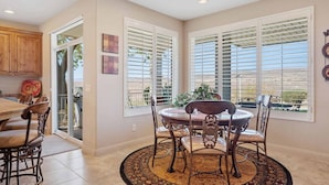 A dining area with a round table and chairs, large windows with blinds, and a view of the outdoors. - Tuscan Desert Vista #2001 by RedAwning (St. George)