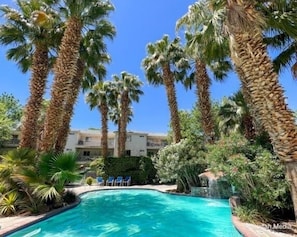 Una piscina rodeada de altas palmeras y un edificio al fondo.