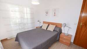 A bedroom with a bed, two bedside tables, a wooden door, and a window with curtains. - A77 HERNANDO I 3º - G (Calpe)