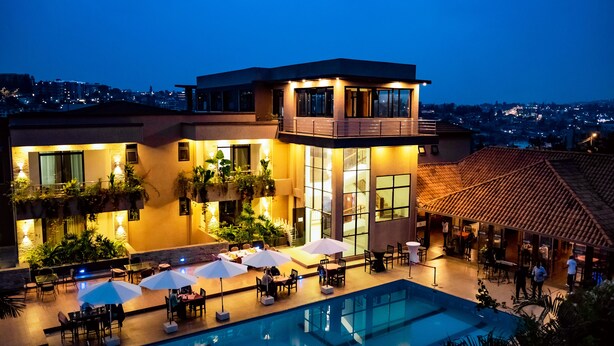 Ein modernes Hotel mit Dachpool, Essbereich im Freien und Blick auf die Stadt bei Dämmerung.