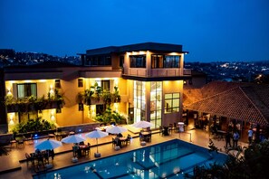 A modern hotel with a rooftop pool, outdoor dining area, and a view of the cityscape at dusk. - GRAZIA HOTEL & APARTMENTS (Kigali)